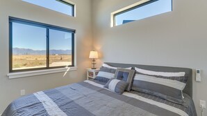 A bedroom with a large bed, two windows, a bedside lamp, and a view of mountains. - "the Farmhouse": Near Flathead Lake & Skiing (Kalispell)