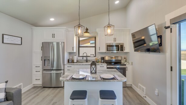 A modern kitchen with white cabinetry, stainless steel appliances, and a central island with stools. - "the Farmhouse": Near Flathead Lake & Skiing (Kalispell)