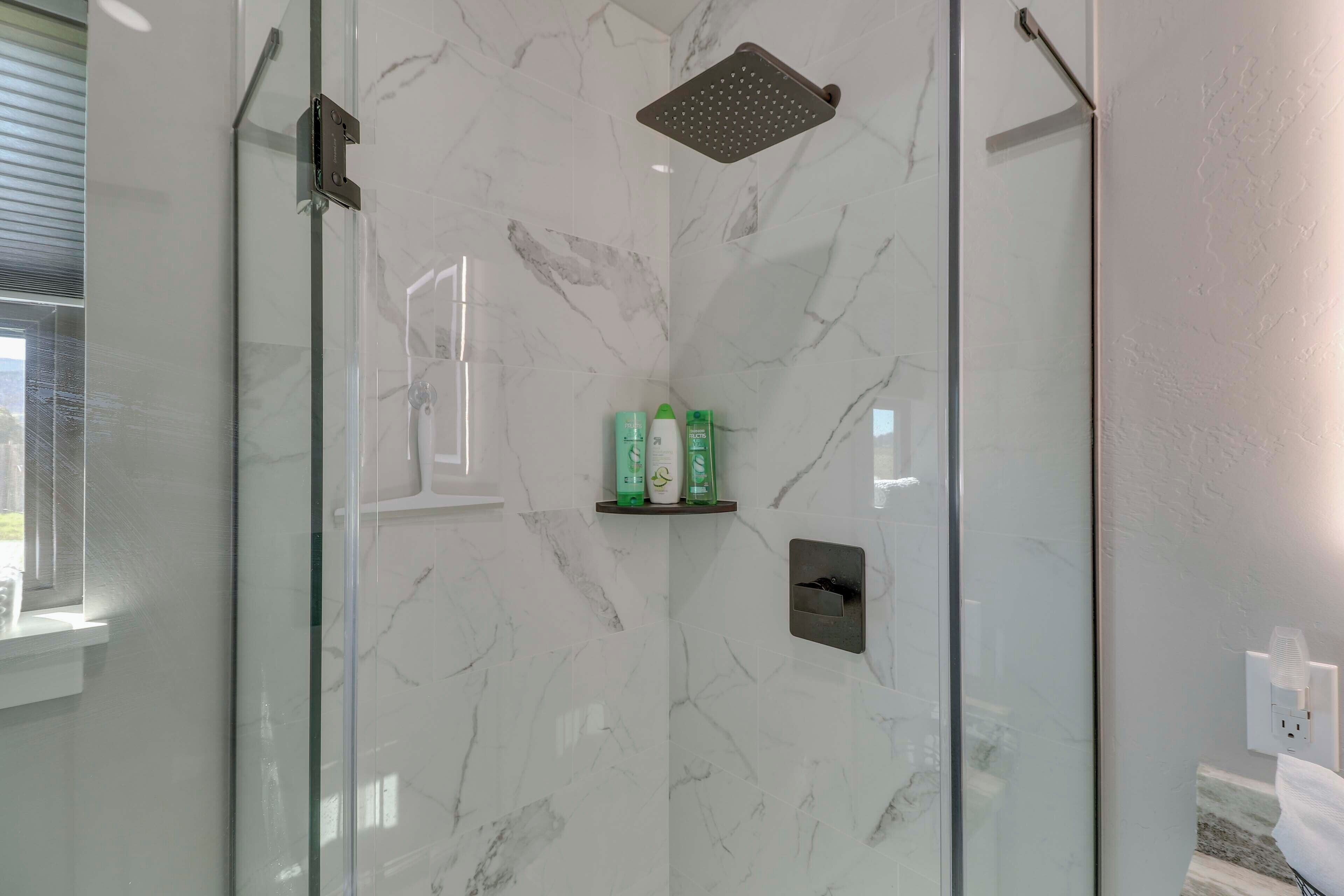 Une douche moderne dotée d’une porte en verre, de murs en marbre et d’une étagère pour les articles de toilette.