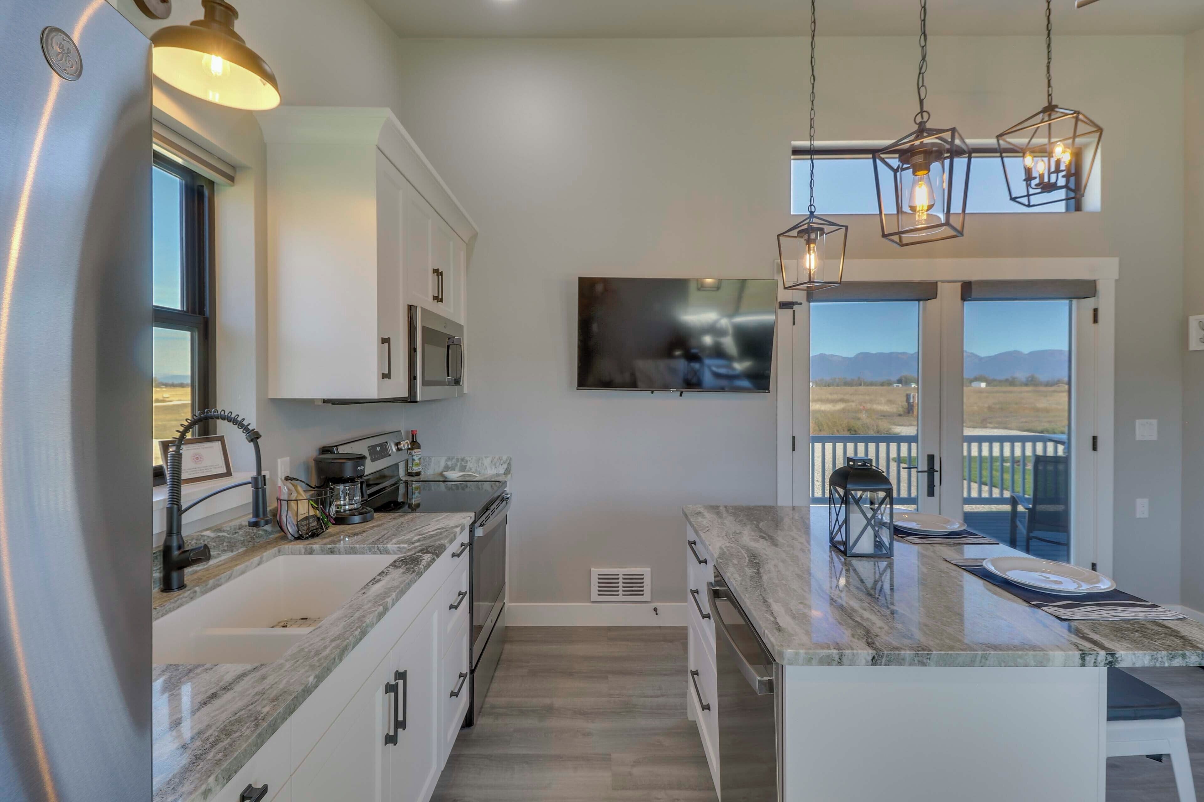 A modern kitchen with white cabinets, a large island, and a flat-screen TV.