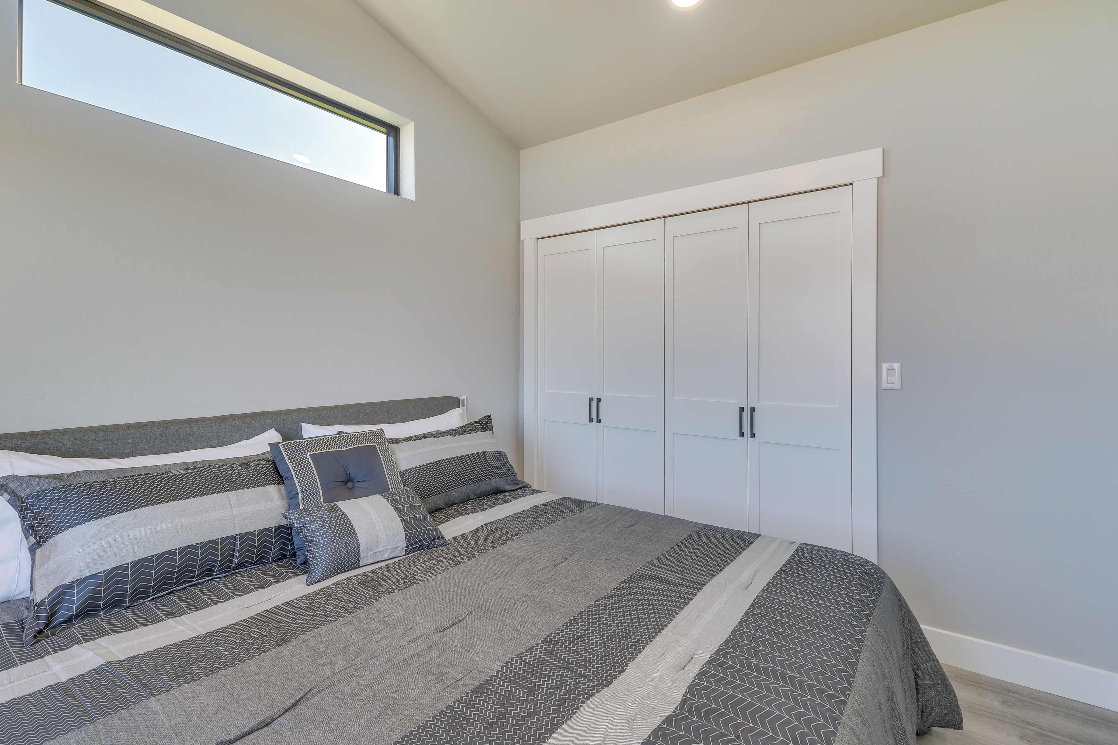 A bedroom with a bed, grey and white bedding, a wardrobe, and a window.