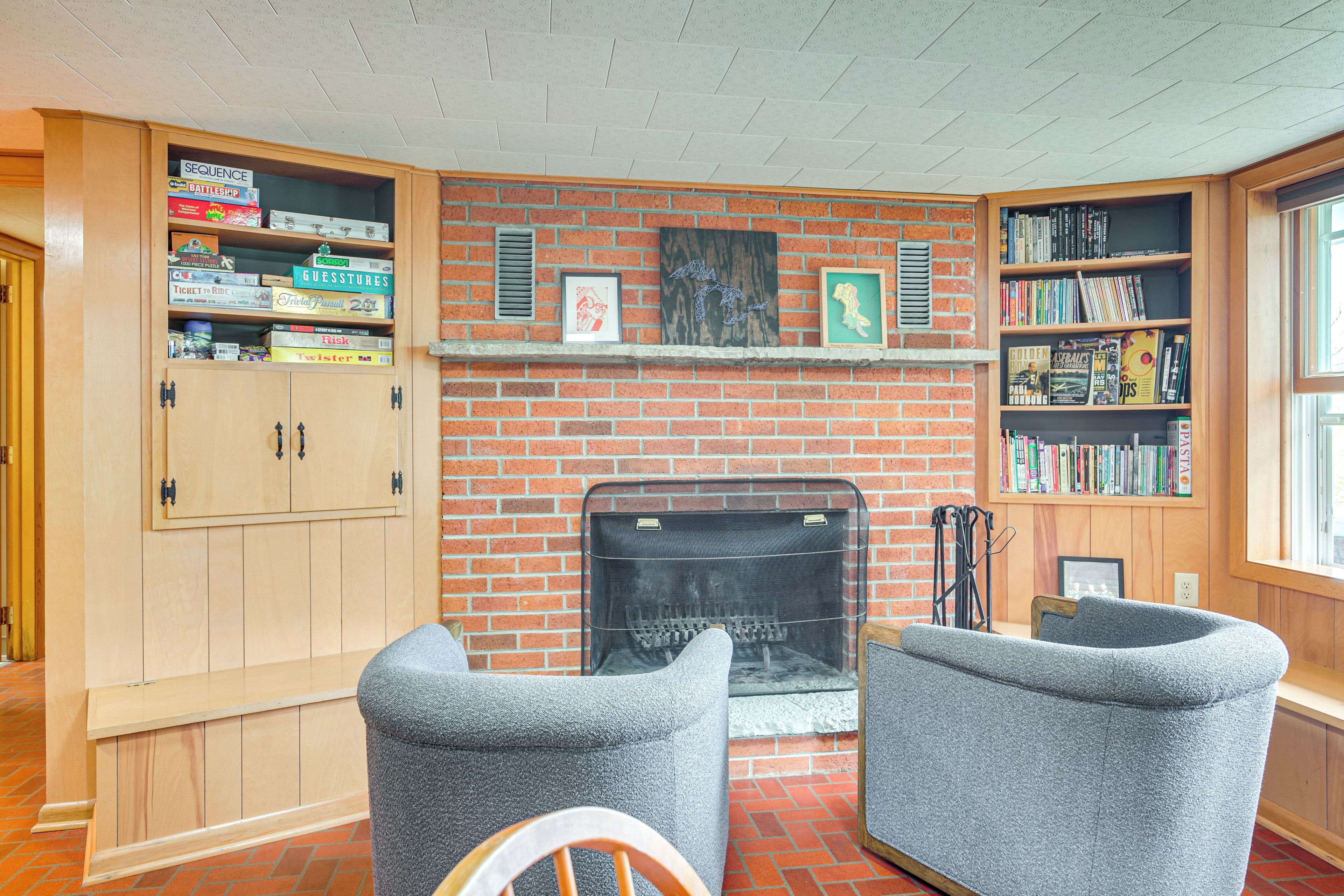 Ein gemütliches Wohnzimmer mit Kamin aus Backsteinen, einem Bücherregal und zwei grauen Sesseln.