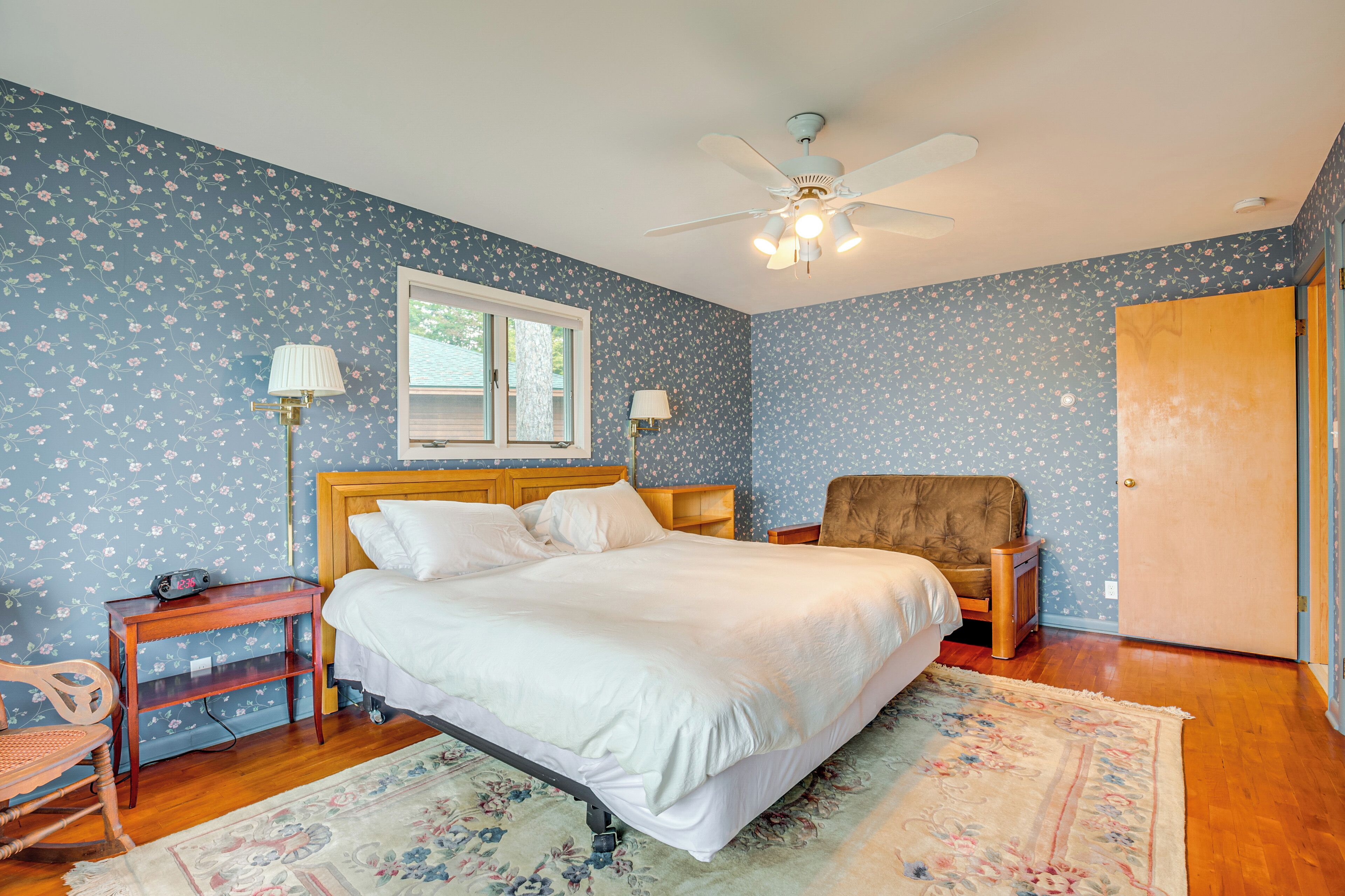A bedroom with a bed, a wooden nightstand, a chair, a ceiling fan, and a door.
