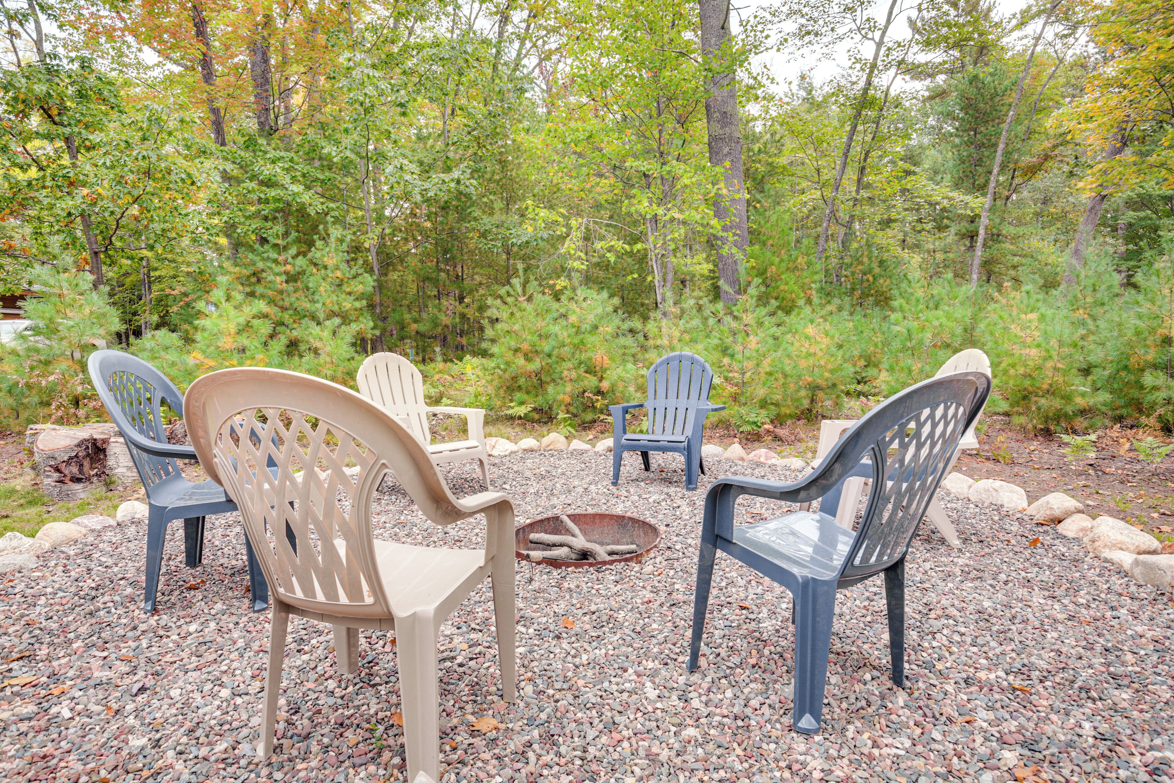 A seating area with chairs arranged around a fire pit, surrounded by a gravel path and trees.