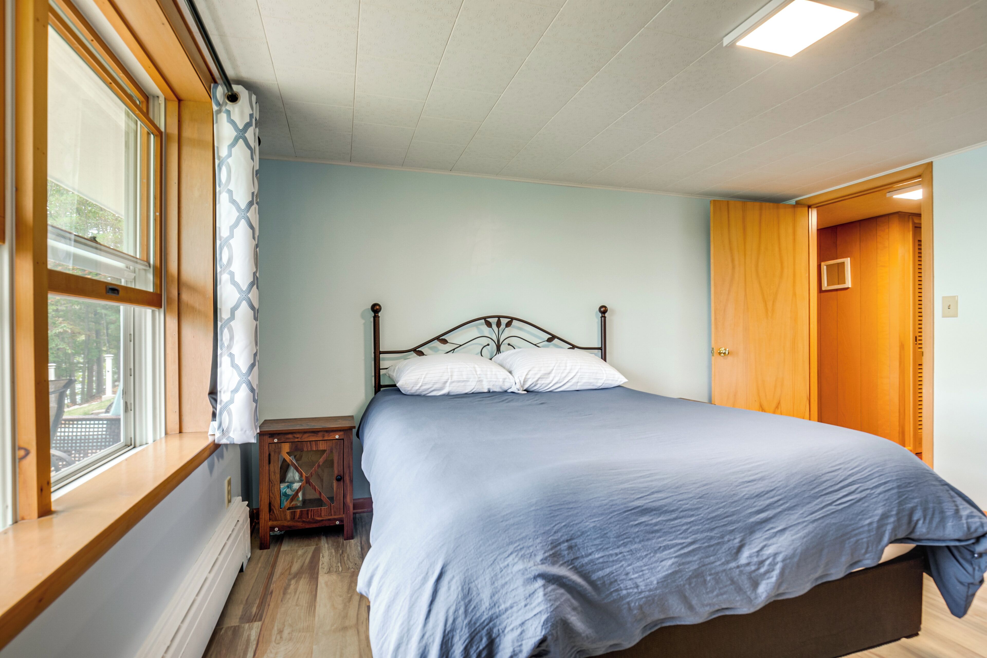 Une chambre à coucher avec un lit, une fenêtre avec des rideaux, une table de chevet en bois et une porte.