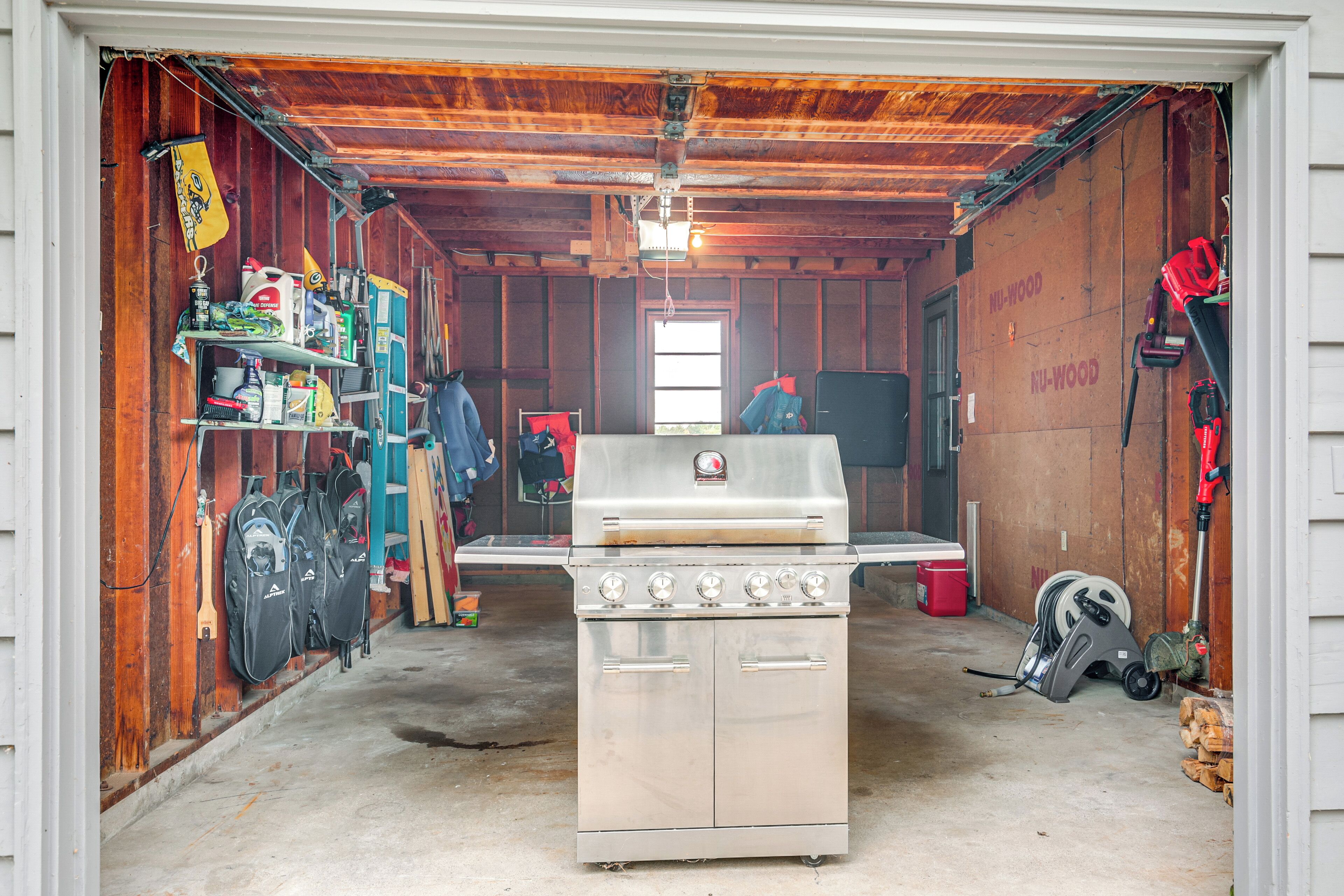 A garage with a stainless steel stove, shelves with tools, and a red tool hanging on the wall.