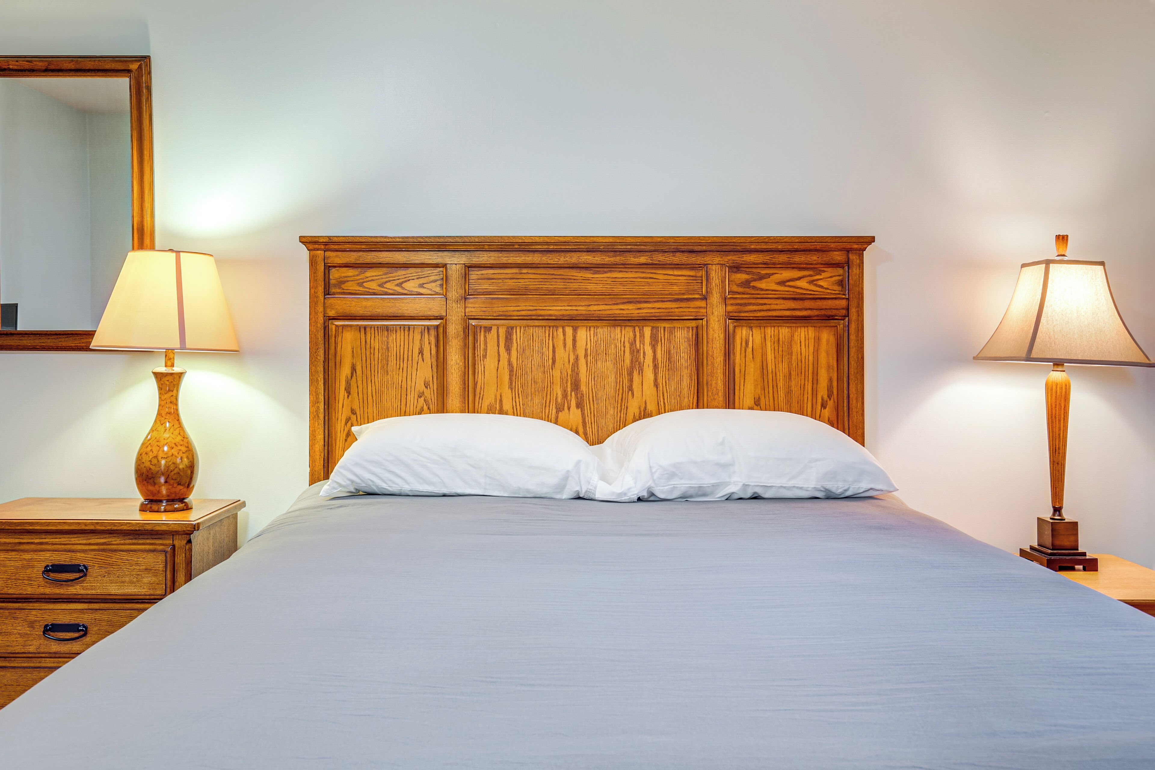 Un letto rifatto con cura, una testiera in legno, due comodini con lampade e uno specchio a parete.