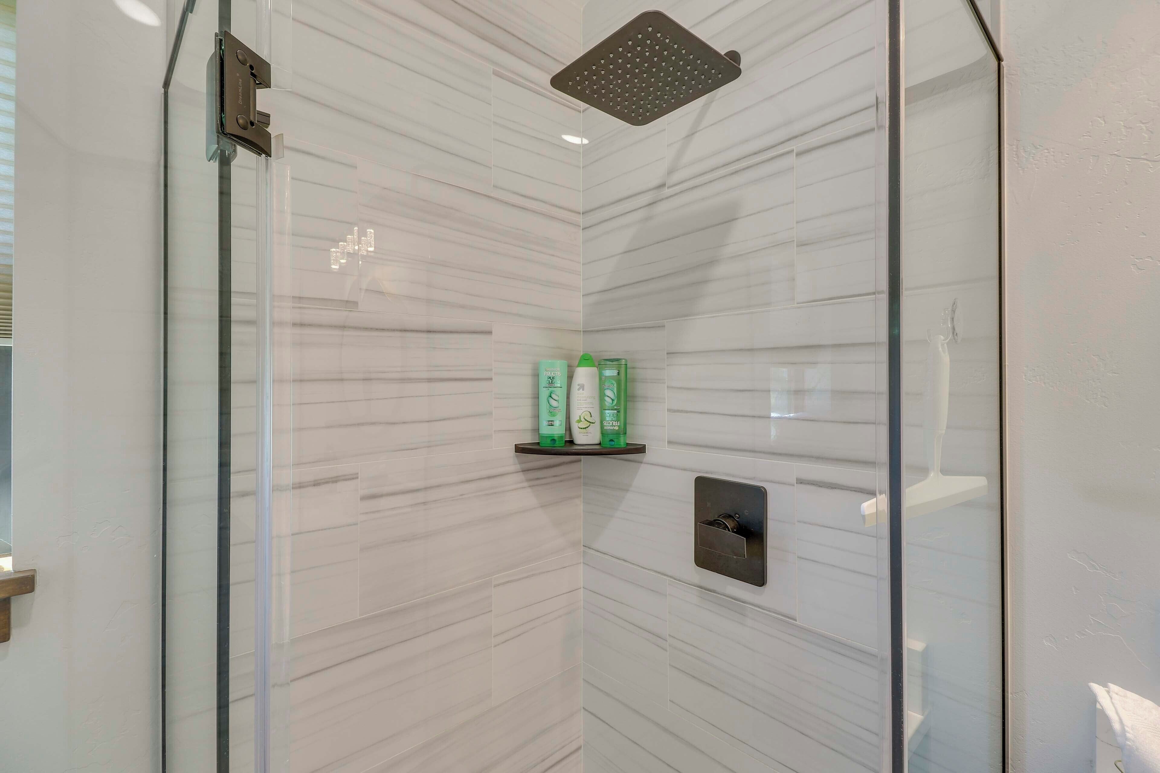 A glass-enclosed shower with a rain showerhead, a shelf with toiletries, and a control panel.