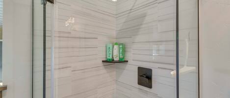 A glass-enclosed shower with a rain showerhead, a shelf with toiletries, and a control panel.