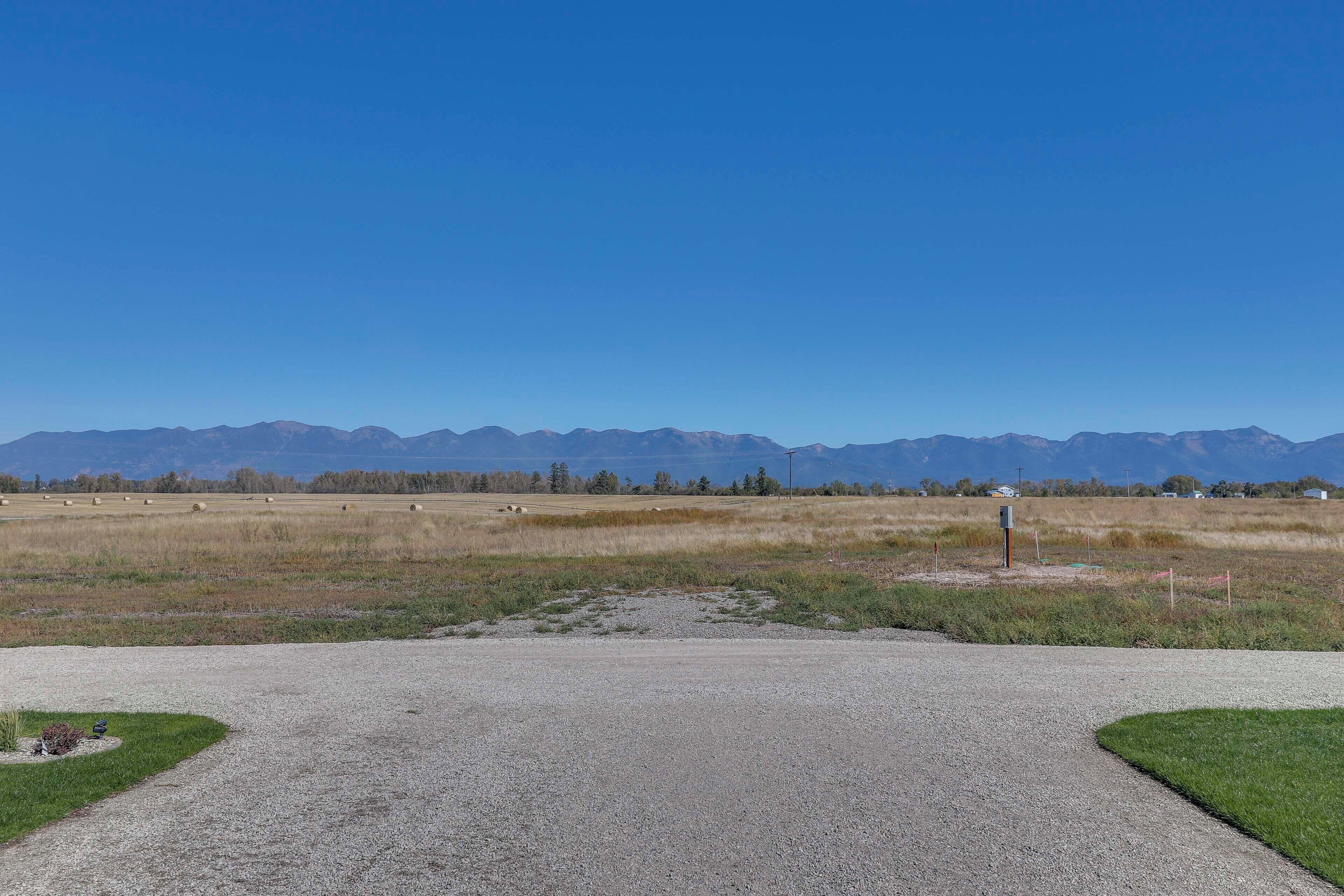 A gravel road leading to a grassy area with mountains in the background.