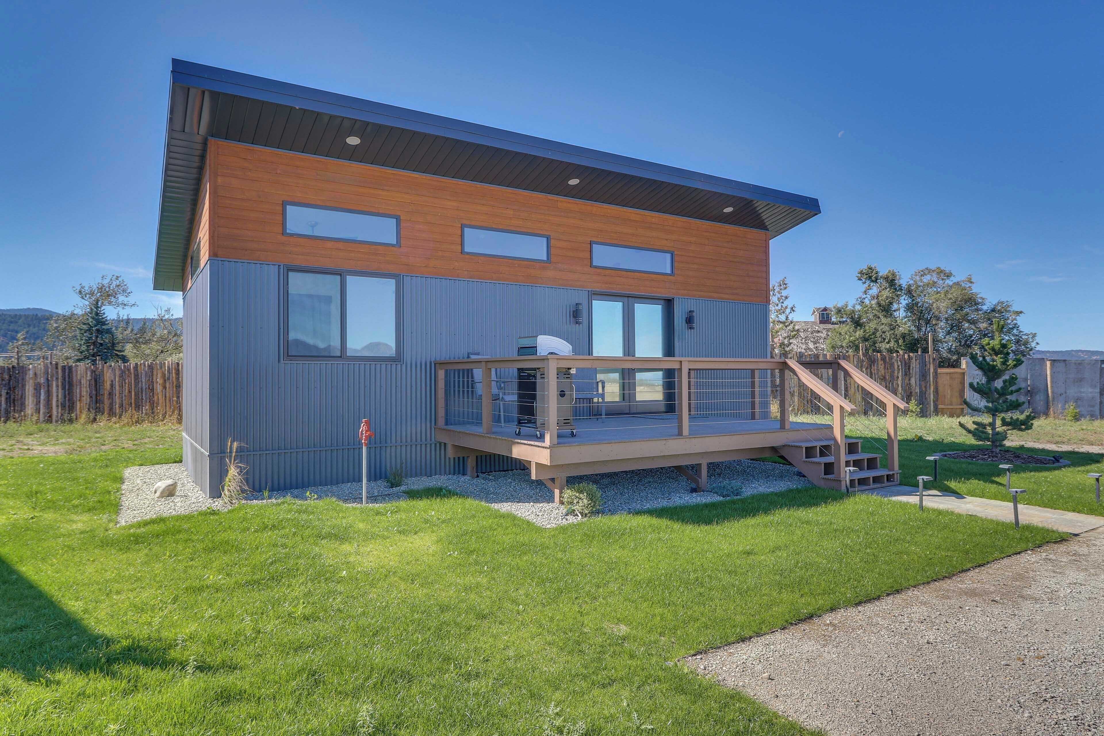 Une maison moderne à deux étages, dotée d’une terrasse en bois et d’un petit escalier menant à un balcon.