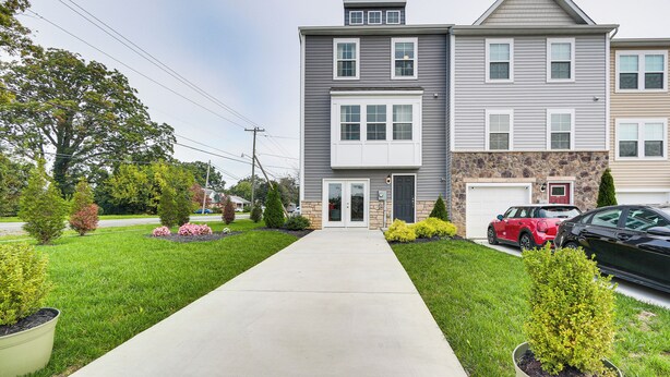 A two-story residential building with a front driveway, a garage, and a well-maintained lawn with various shrubs and flowers.