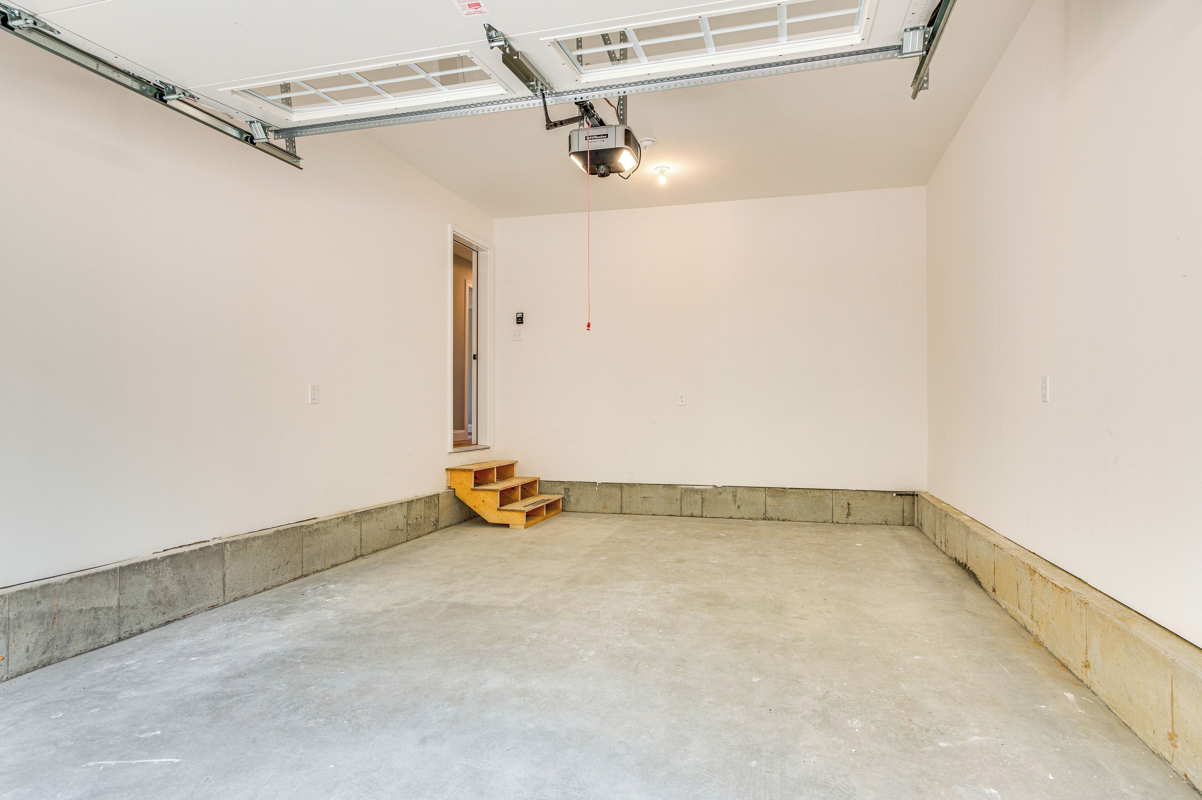 Une grande pièce vide, dotée d’un sol en béton, d’un escalier en bois et d’un projecteur fixé au plafond.