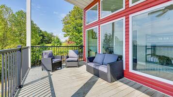A covered outdoor deck with wicker furniture and large windows.
