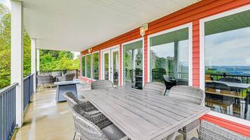 A covered patio with a table and chairs, large windows, and a view of greenery.