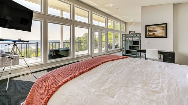 Un dormitorio amplio con una cama grande, varias ventanas, un balcón y un espacio de escritorio.