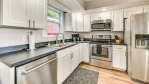 Una cocina moderna con electrodomésticos de acero inoxidable, armarios blancos y encimera de granito.