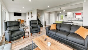 Una sala de estar moderna con un sofá, sillones y una mesita de centro. Una escalera conduce al piso superior.