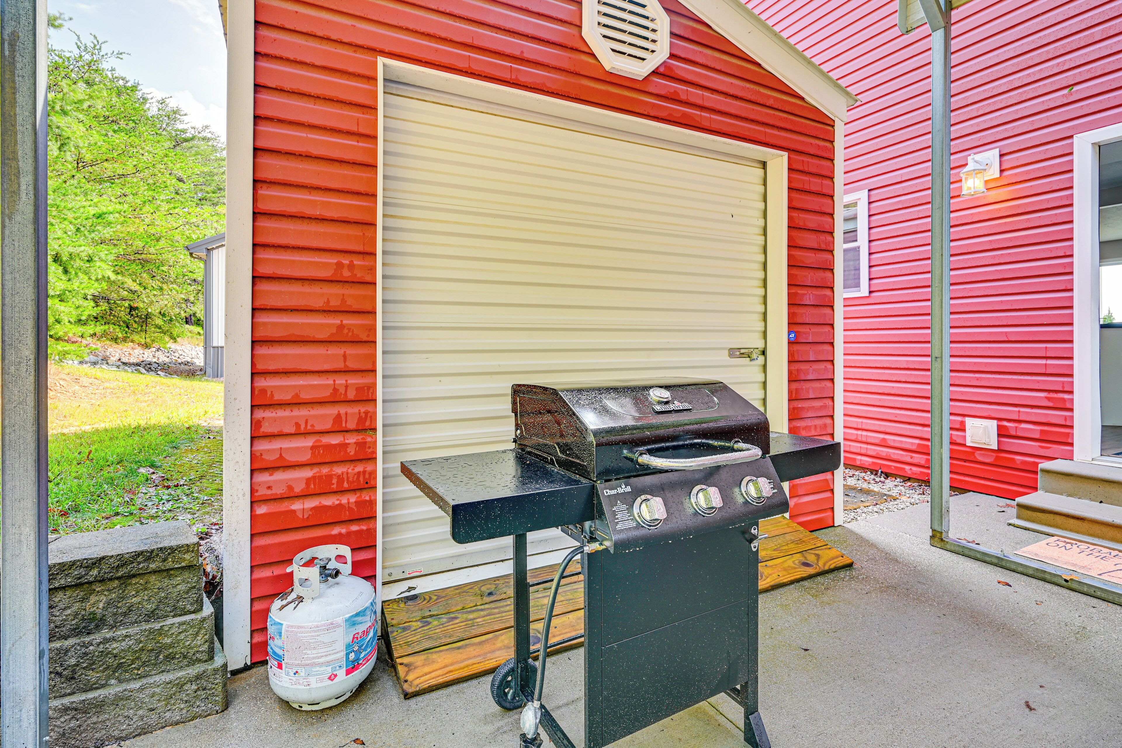 A red building with a closed garage door, a barbecue grill, and a propane tank outside.
