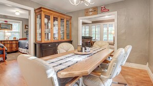 A dining area with a long wooden table, cushioned chairs, a chandelier, and a cabinet with glass doors. - Hillside Home on 4 Wooded Acres by Sunday Lake (Wakefield)