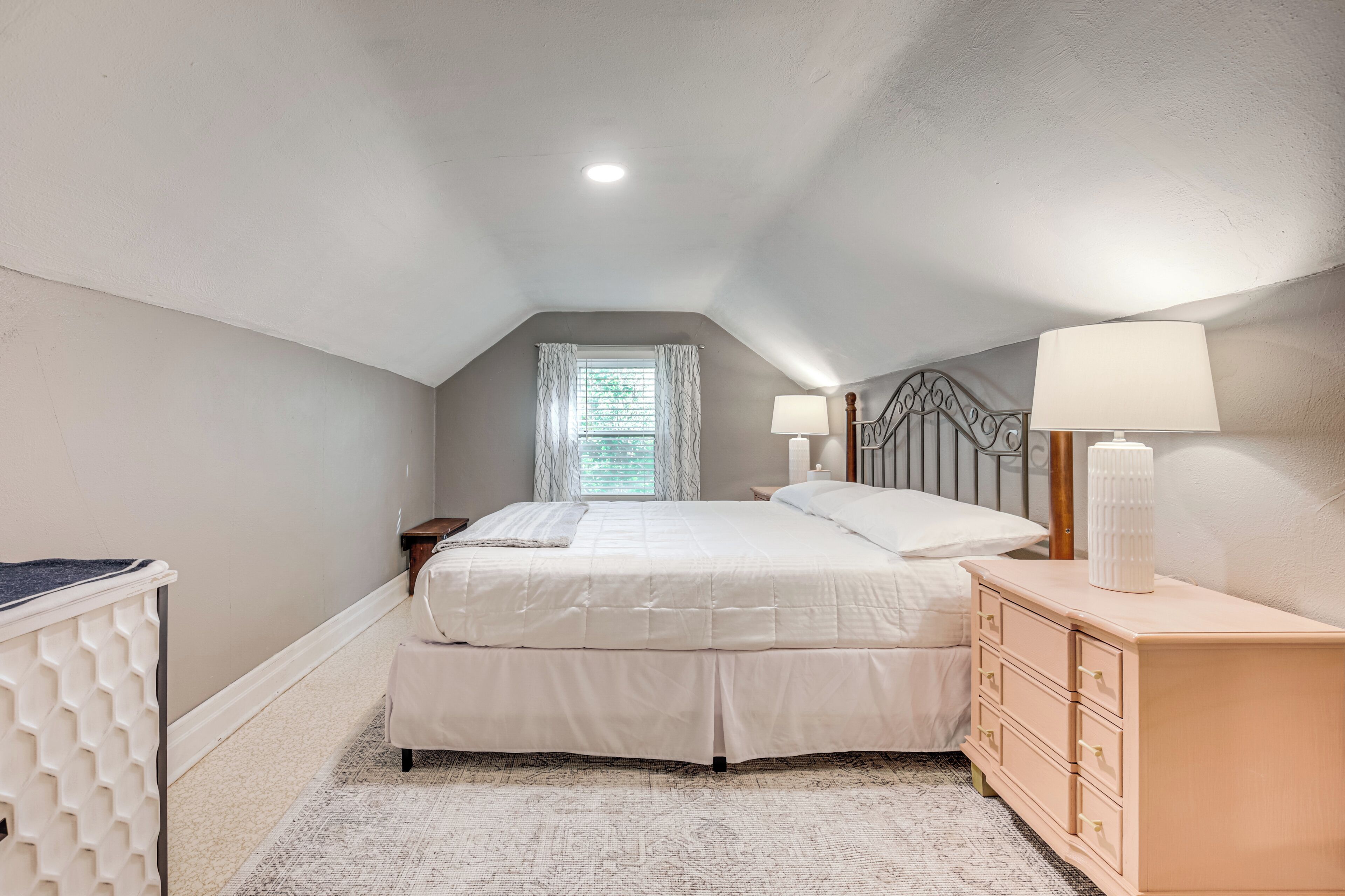 Une chambre à coucher avec un lit, des tables de chevet, une commode et une fenêtre avec des rideaux.