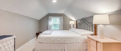 Une chambre à coucher avec un lit, des tables de chevet, une commode et une fenêtre avec des rideaux.