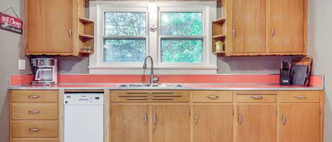 A kitchen with wooden cabinets, a dishwasher, and a window with a view of trees.