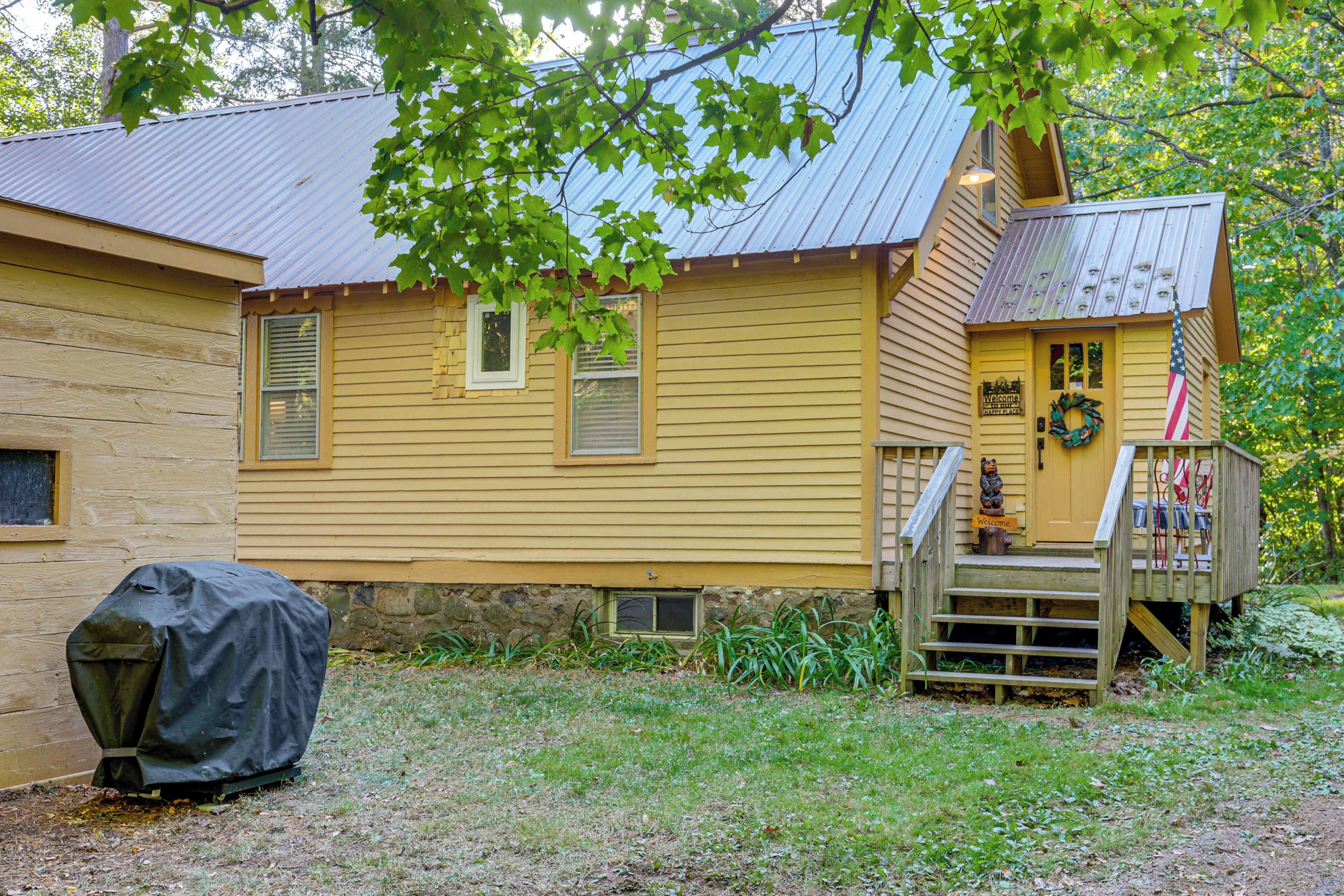 A yellow wooden house with a porch, a covered grill, and a small staircase leading to the entrance.