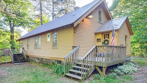 A wooden cabin with a porch, a flag, and a staircase leading to the entrance. - Hillside Home on 4 Wooded Acres by Sunday Lake (Wakefield)