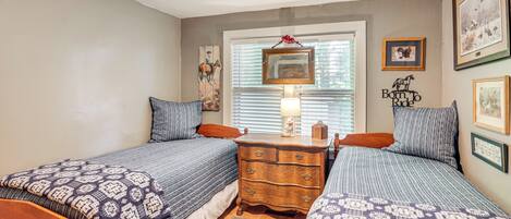 A bedroom with two beds, a dresser, and a window with blinds.