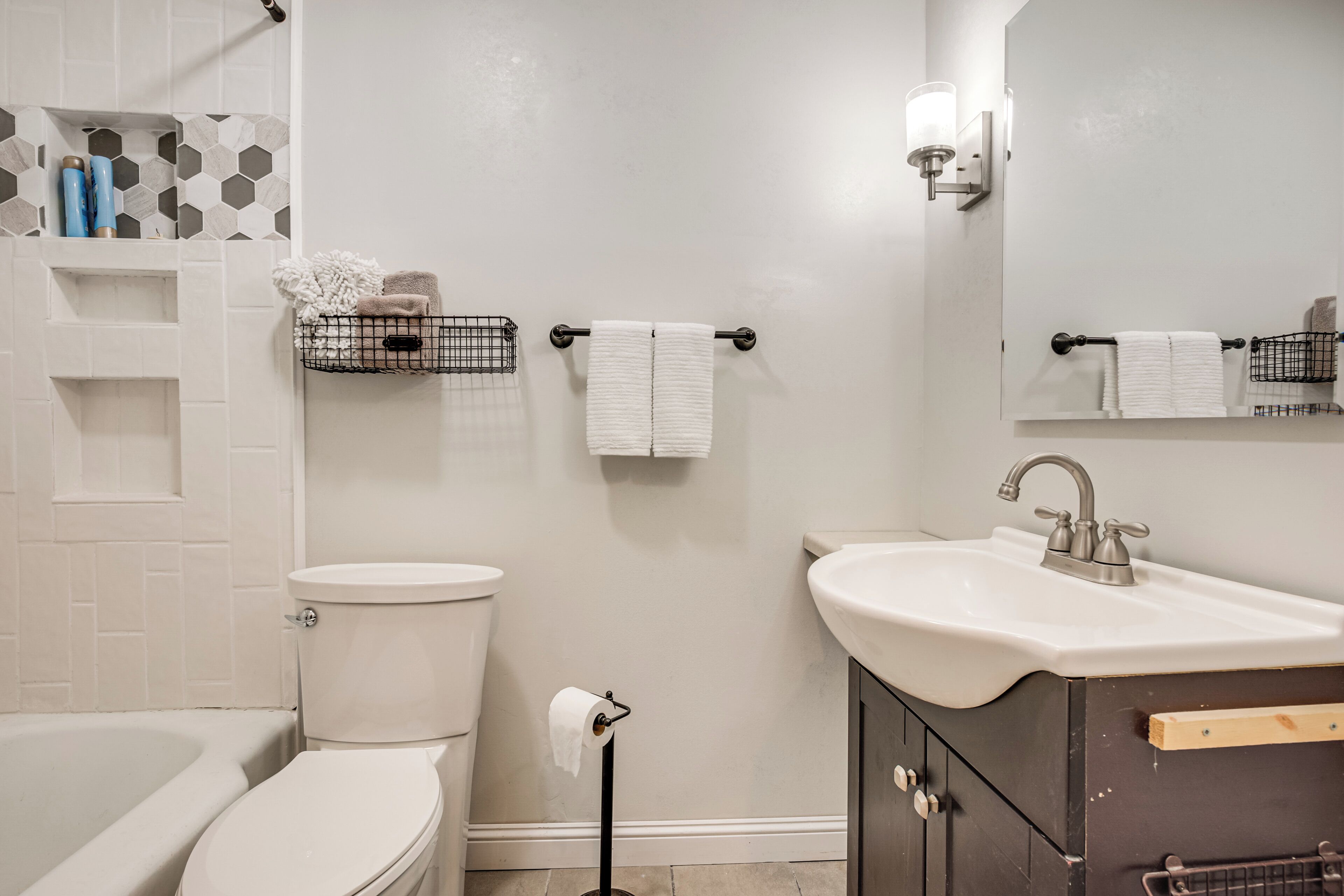 Ein modernes Badezimmer mit Toilette, Waschbecken und Badewanne. Handtücher hängen an einem Wäscheständer und über dem Waschbecken befindet sich ein Spiegel.