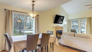 A dining area with a table and chairs, a fireplace, and a sofa in a living room with large windows.