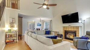 A spacious living room with a large sofa, a fireplace, a television, and a bookshelf.