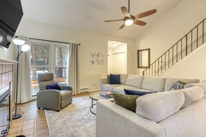 A living room with a grey sofa, a small armchair, a coffee table, and a ceiling fan. There is a staircase with a railing leading to an upper level. - 11 Miles to Saratoga Race Course: Upstate Retreat! (Ballston Spa)
