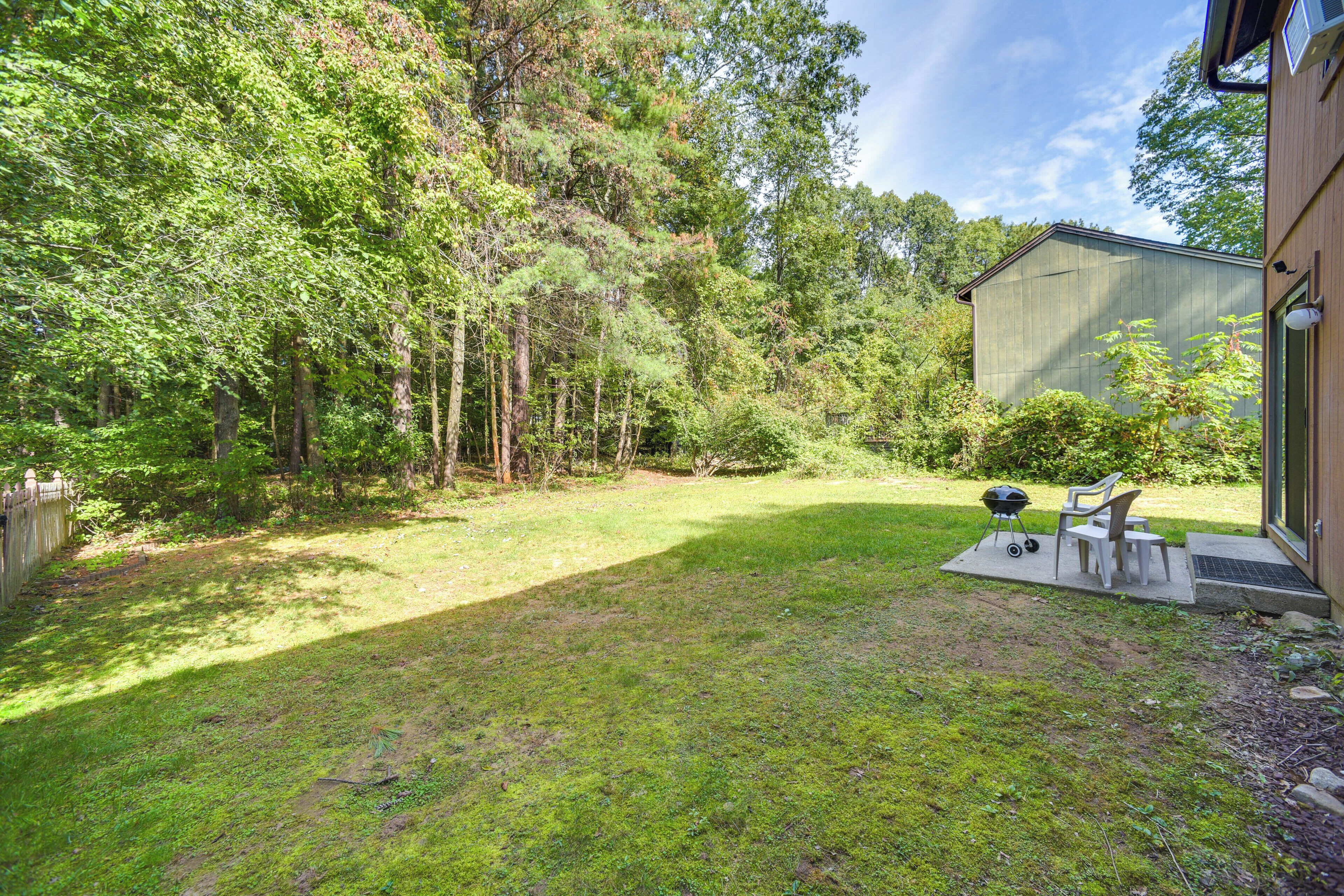 A backyard with a grassy lawn, a barbecue grill, and two chairs.