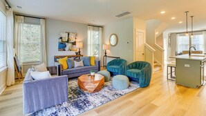 A spacious living room with a sofa, ottomans, a coffee table, and a dining area with a kitchen counter. - 13 Mi to Dtwn Charleston: Quiet Townhome (Hanahan)