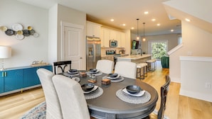 A modern kitchen with white cabinets, a stainless steel refrigerator, and a microwave. There is a dining area with a round table set for four, surrounded by chairs. - 13 Mi to Dtwn Charleston: Quiet Townhome (Hanahan)