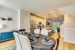 A modern kitchen with white cabinets, a stainless steel refrigerator, and a microwave. There is a dining area with a round table set for four, surrounded by chairs.