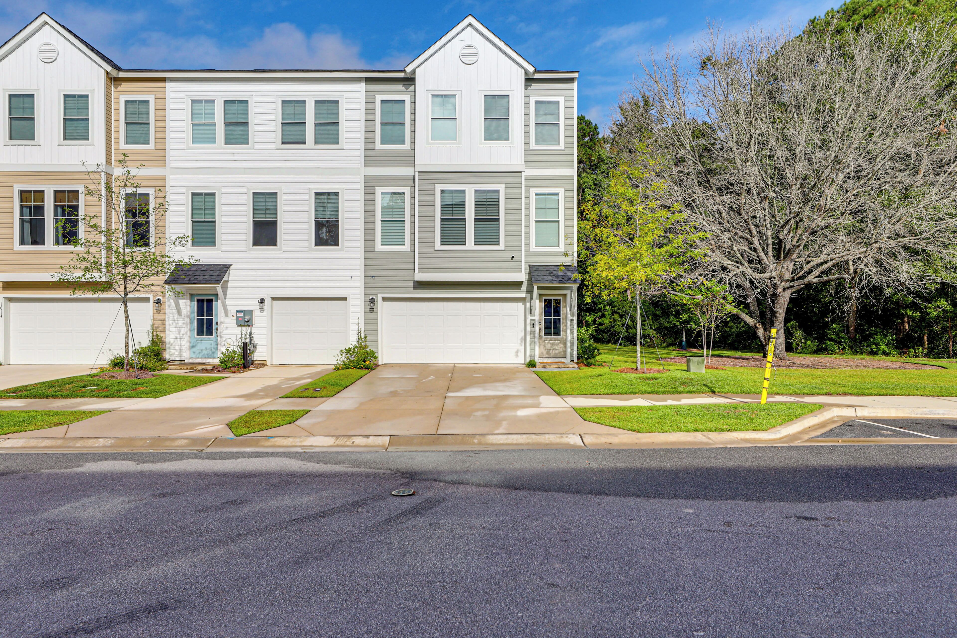 A multi-story residential building with a garage, a well-maintained lawn, and a tree in the front yard.