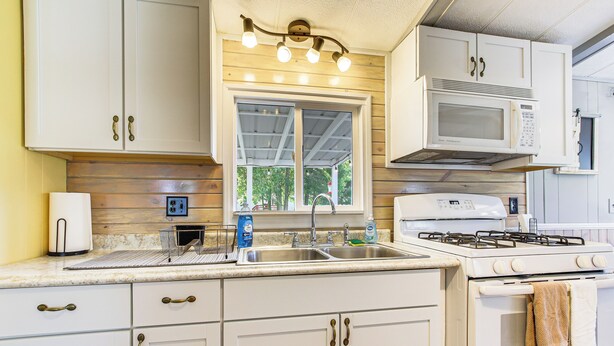 A kitchen with white cabinets, a stainless steel sink, a microwave, and a stove. - Lake Views & Fireside Bliss: Cecil Cottage w/ Yard (Cecil)