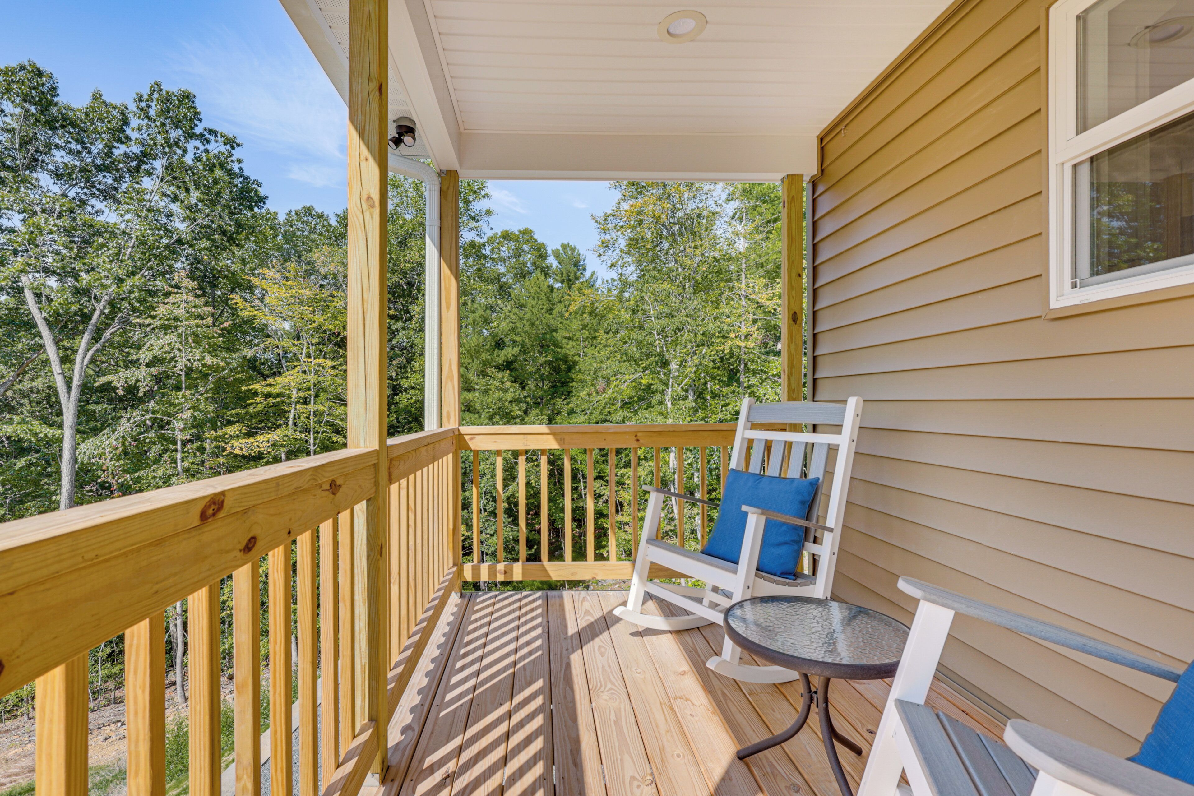 A wooden deck with a rocking chair and a small table, overlooking a forested area.