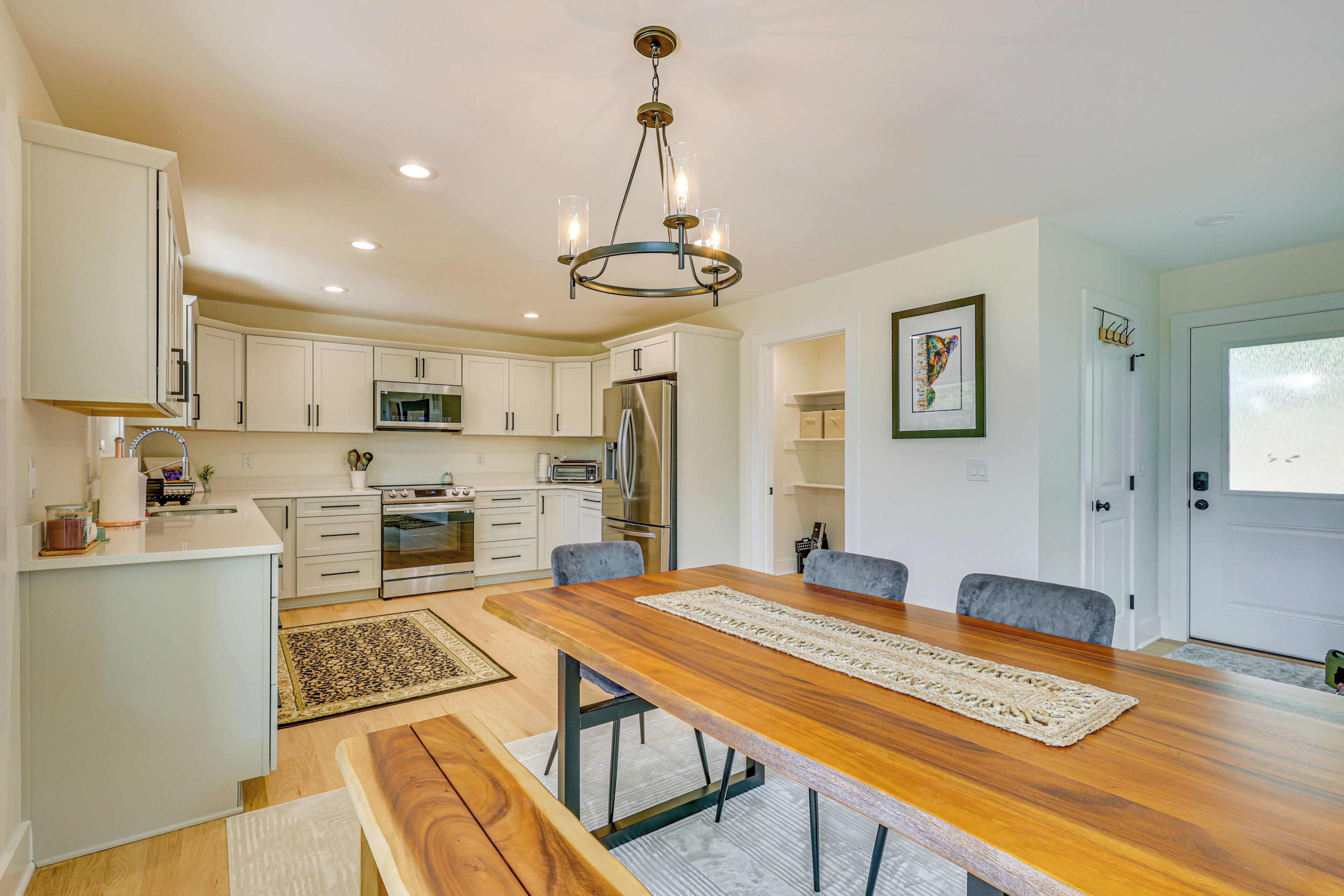 A modern kitchen with white cabinets, a wooden dining table, and a chandelier.