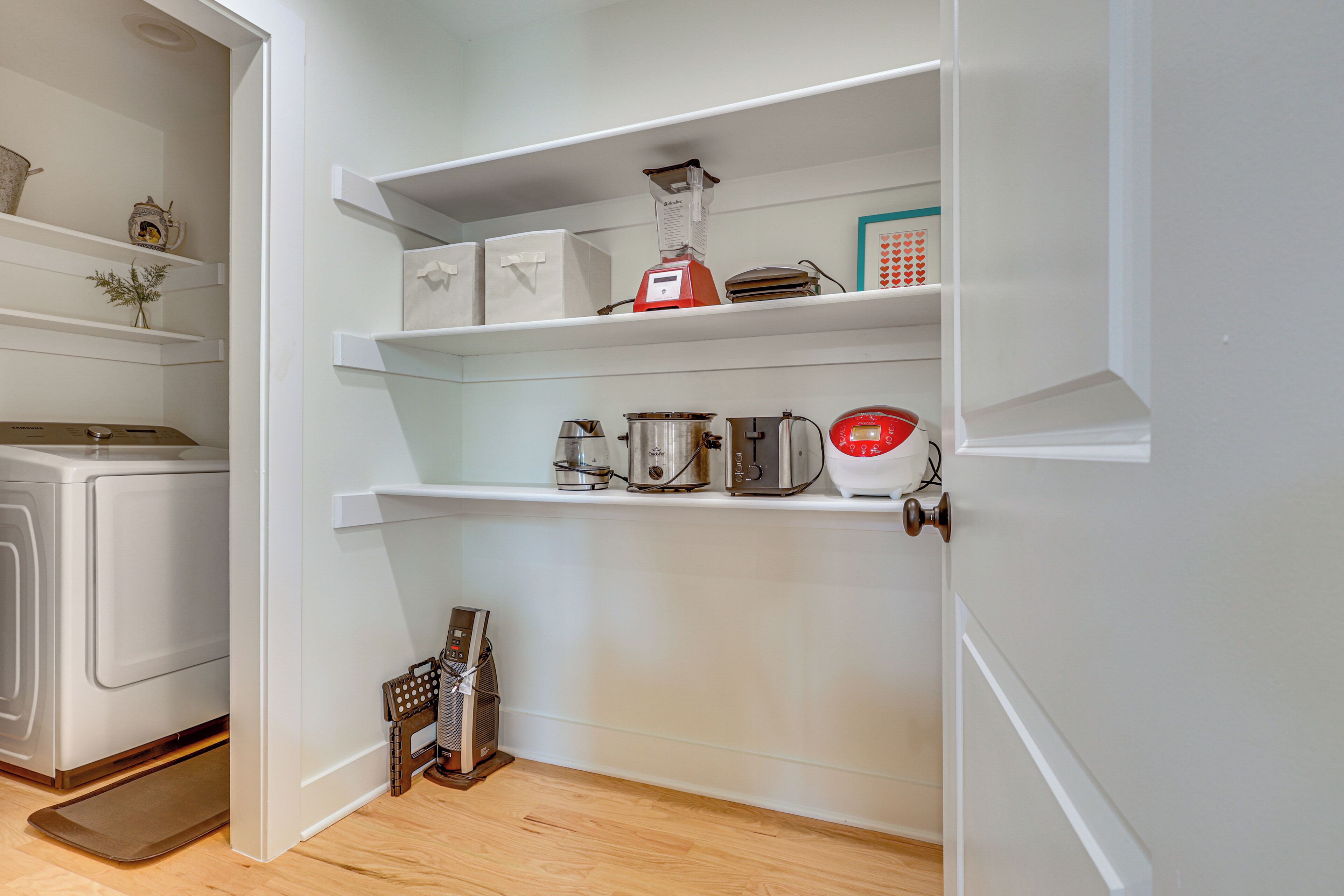 A compact kitchen with white cabinetry, a coffee maker, a blender, and a toaster on the shelves.