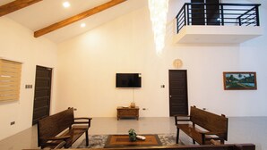 A spacious living room with wooden furniture, a flat-screen TV, and a balcony. - GAVs Abode: Your Spacious and Peaceful home in Duma (Dumaguete)