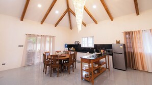 A spacious kitchen with wooden beams, a chandelier, a dining area with chairs, and a refrigerator. - GAVs Abode: Your Spacious and Peaceful home in Duma (Dumaguete)