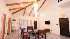 A spacious room with wooden beams, a chandelier, a dining table with chairs, a television, and a clock on the wall. - GAVs Abode: Your Spacious and Peaceful home in Duma (Dumaguete)