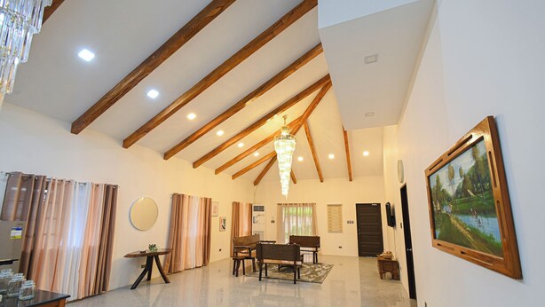 A spacious living area with a high ceiling, wooden beams, a chandelier, a dining table with chairs, and a painting on the wall. - GAVs Abode: Your Spacious and Peaceful home in Duma (Dumaguete)