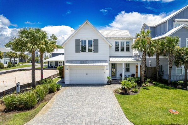 Een tweelaags huis met een witte gevel, een garage en een verharde oprit die naar de voordeur leidt.