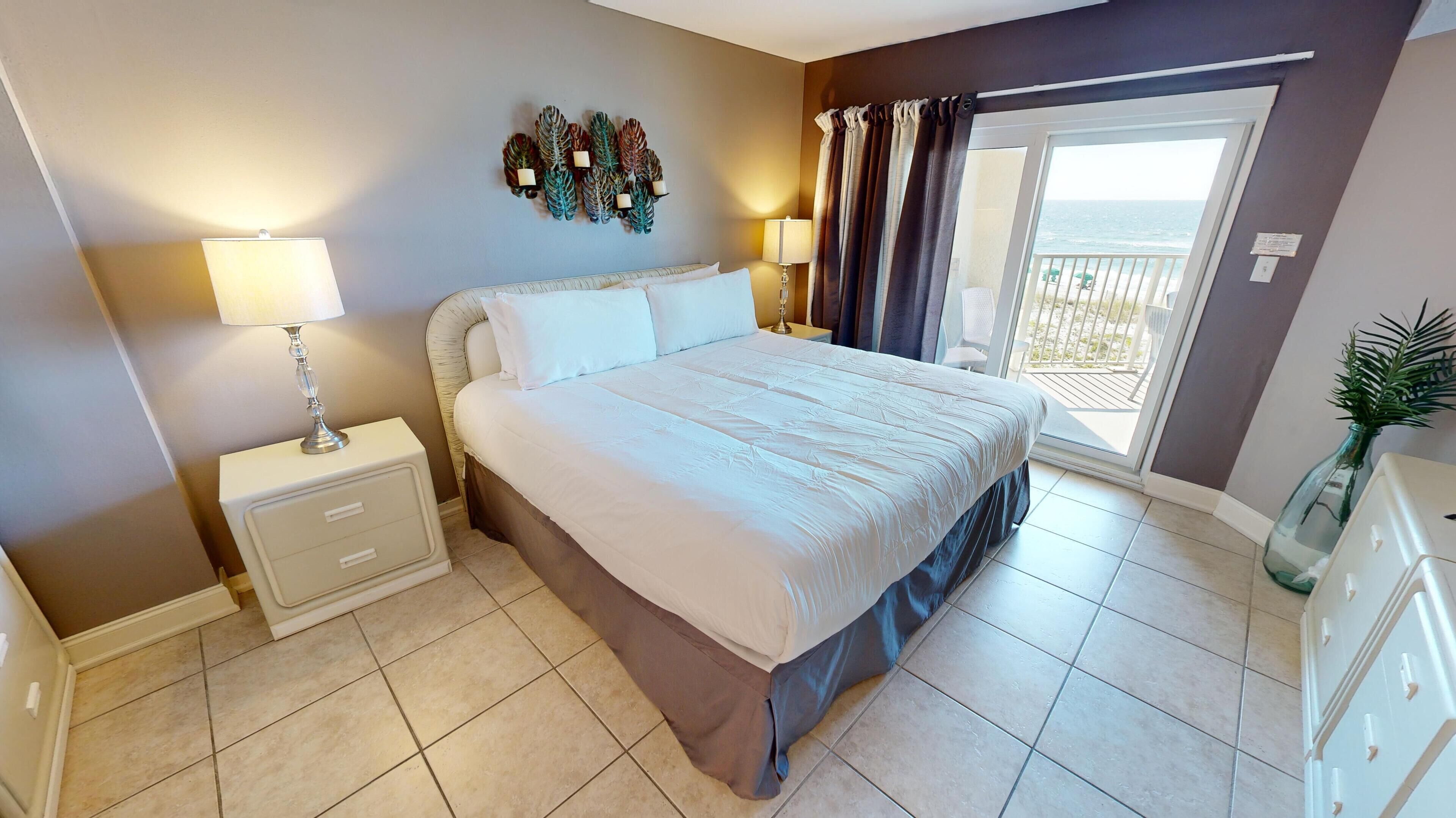 Une chambre à coucher bien aménagée, avec un grand lit, deux tables de chevet dotées de lampes, un élément décoratif mural et une vue sur l’extérieur grâce à une porte coulissante.