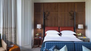 Une chambre d’hôtel avec une tête de lit en bois, un lit avec du linge de lit blanc, un canapé bleu, une petite table avec une lampe et une chaise.